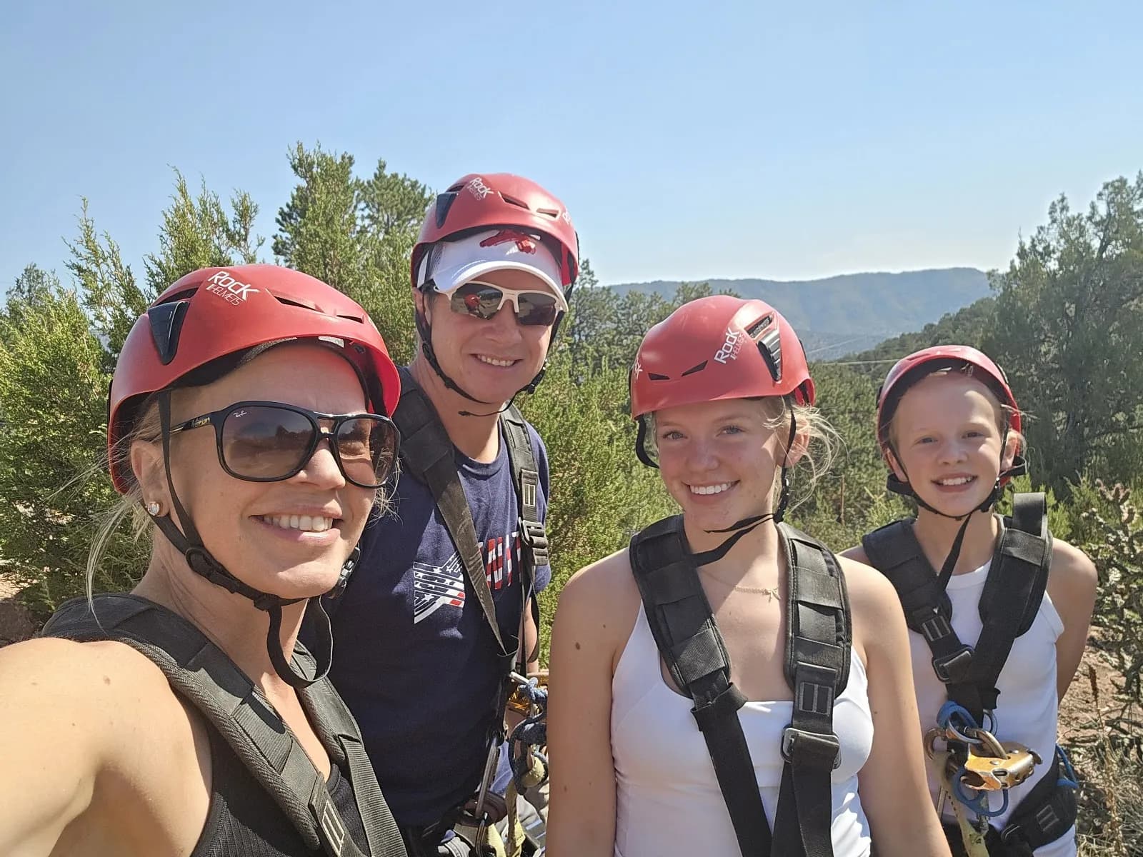 Guest photo by Sheri on Google: a smiling family of four in red helmets and harnesses on the zip line course